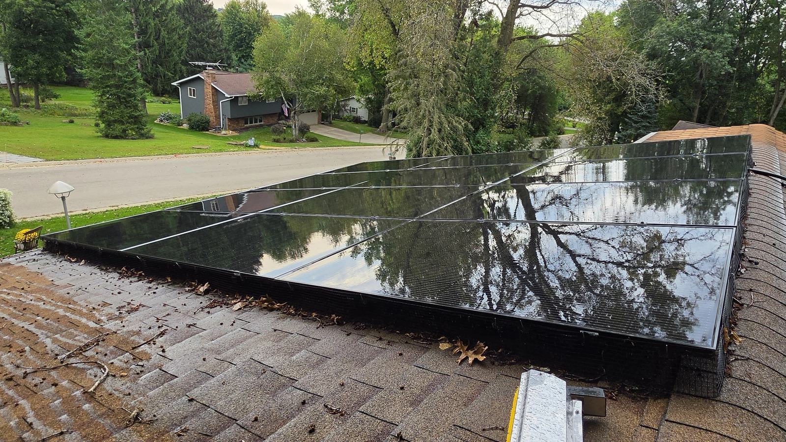 Same Waunakee, Wisconsin residential solar array photographed at 10:02 AM after Solar Alchemist cleaning, glass is mirror-clean and clearly reflects the neighborhood trees, sky, and roofline across the street