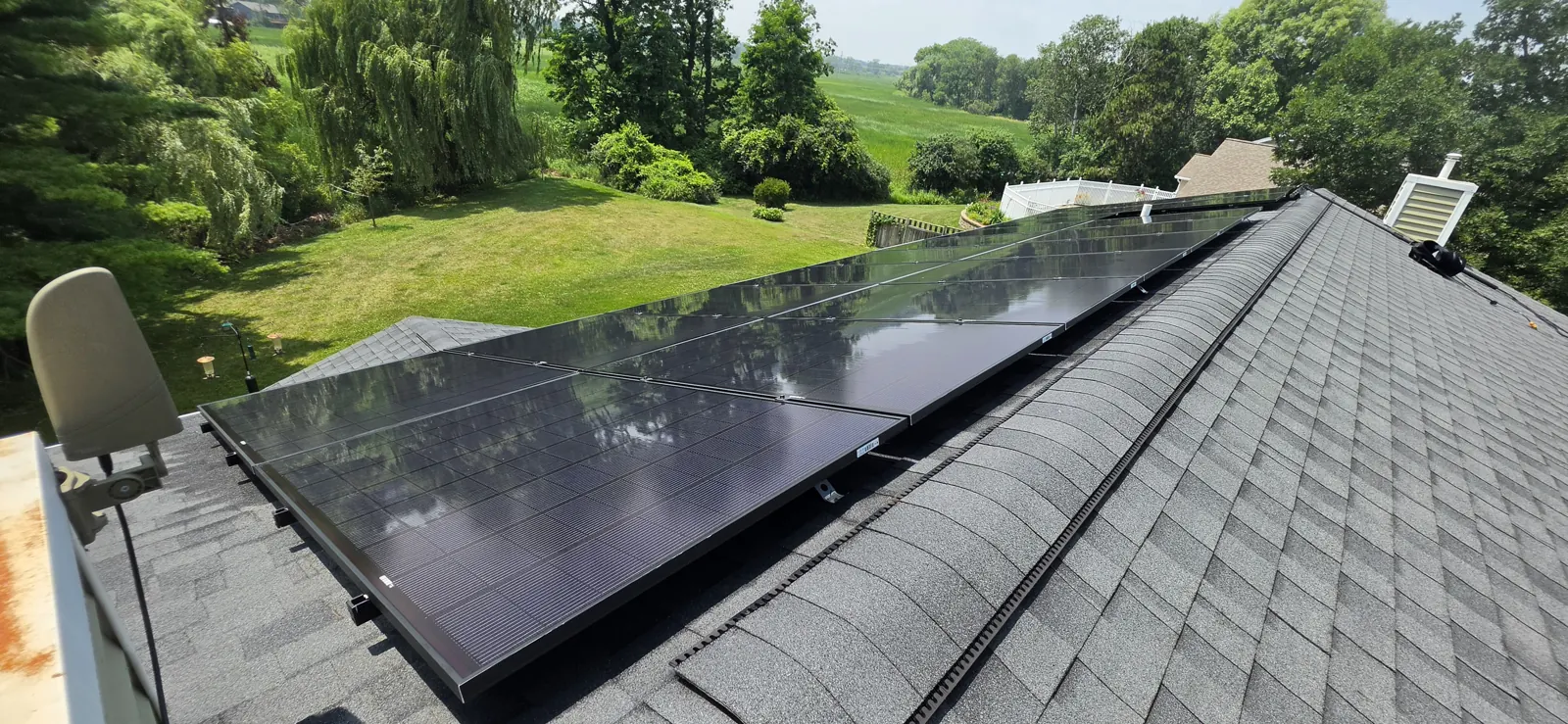 Same rural Southern Wisconsin residential solar array photographed from the opposite roof end after cleaning, with tree canopies reflected in the glass and open cornfields on the horizon