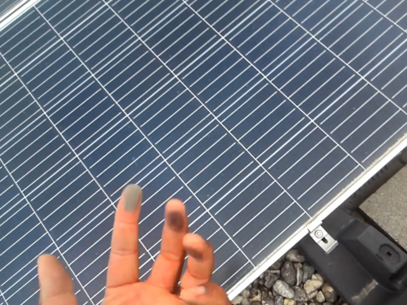 A finger wiped across a commercial solar panel, the clean streak showing the film of dust sitting on the glass
