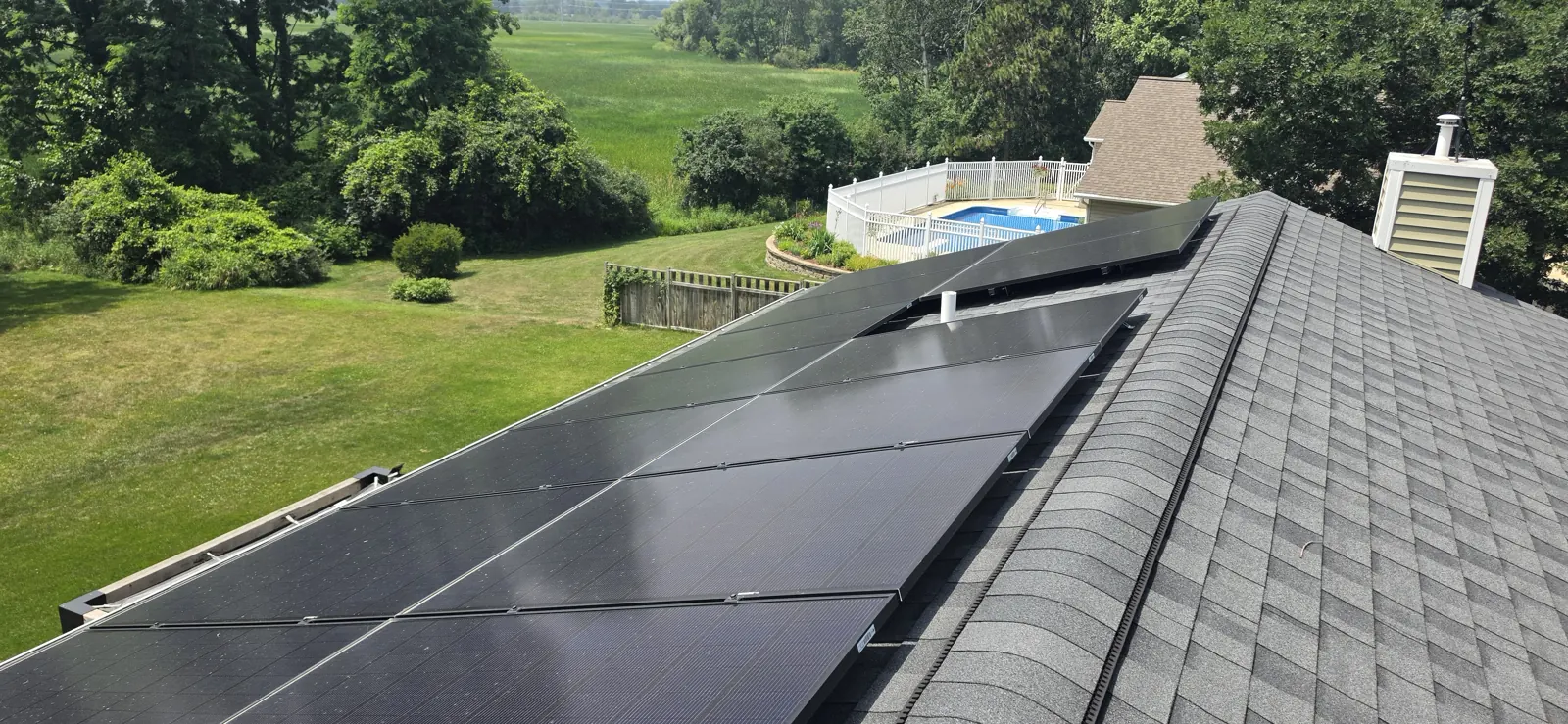 Residential rooftop solar array running along the ridge of a rural Southern Wisconsin home after a Solar Alchemist cleaning, with mature trees, a pool, and surrounding farm fields visible below