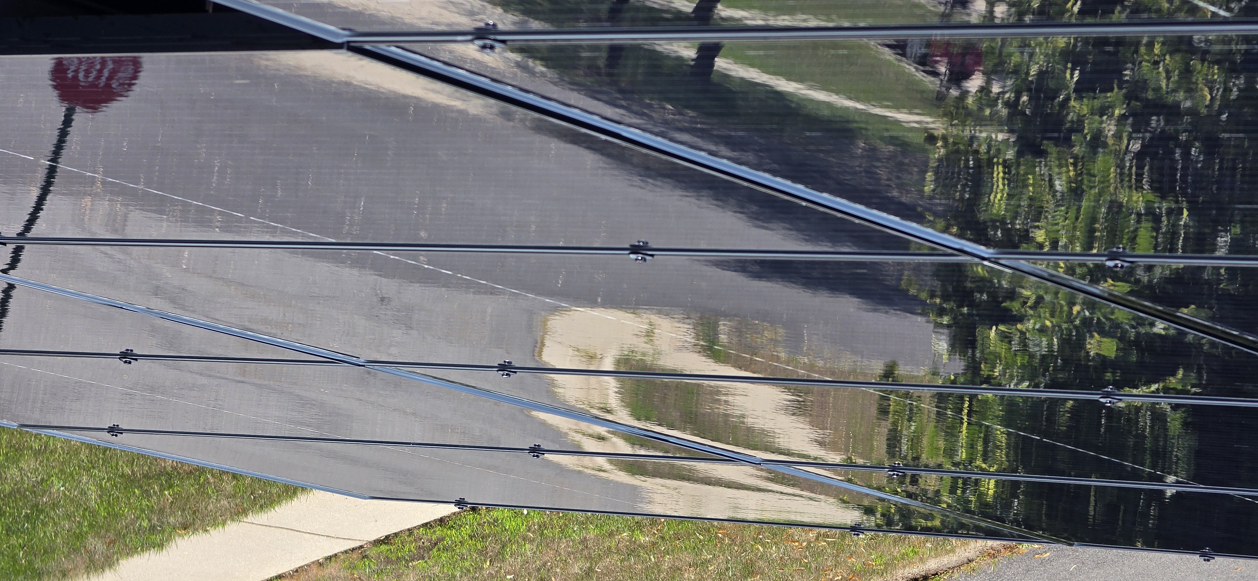 Same front-pitch rooftop solar array after Solar Alchemist cleaning — glass is mirror-clean and clearly reflects the driveway and grass line below